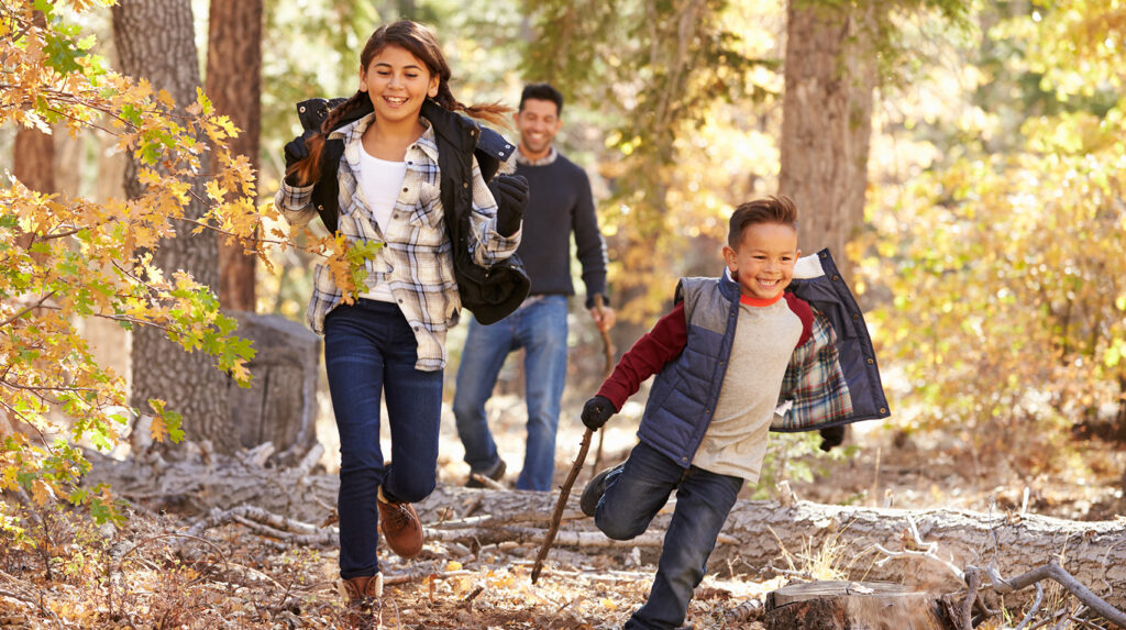 Children in a forest running to camera, father looking on