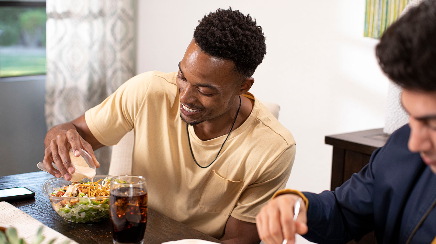 Man pouring chipotle ranch dressing on Rubio's Chopped Salad with Grilled Chicken at dining room table